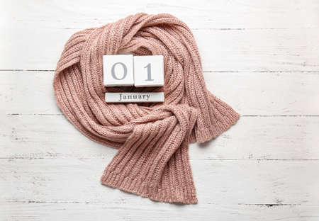 Warm scarf and calendar with date of New Year on wooden background