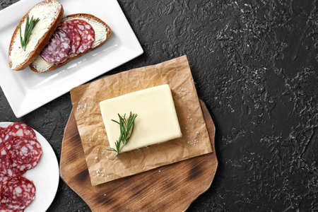 Tasty butter with bread and sausages on dark background