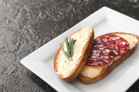 Plate with tasty bread, butter and sausages on dark backgroundの写真素材