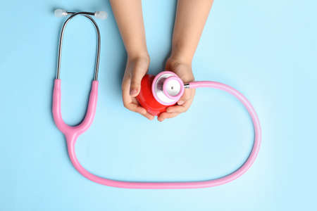 Child hands with red heart and stethoscope on color background. Cardiology conceptの写真素材