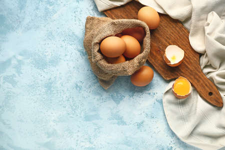 Sack with fresh eggs on color background
