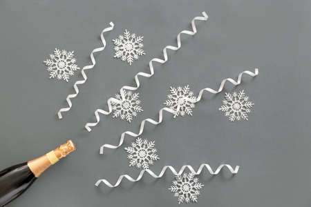 Bottle of champagne with snowflakes and streamers on gray background
