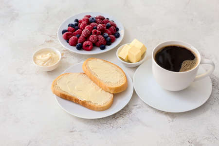 Tasty breakfast with fresh bread, butter, berries and cup of coffee on white backgroundの写真素材