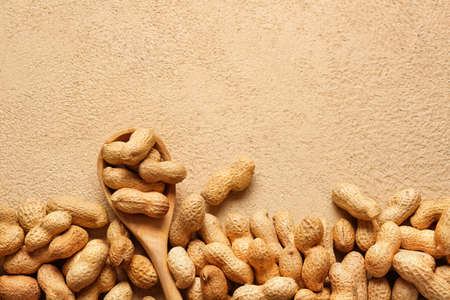 Spoon with peanuts on color background