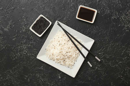 Plate with boiled rice and soy sauce on dark background