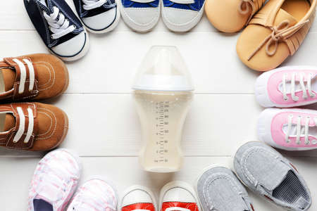 Bottle of milk for baby with shoes on white wooden backgroundの写真素材