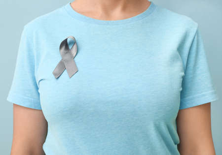 Woman with Parkinson's awareness ribbon on color background, closeup
