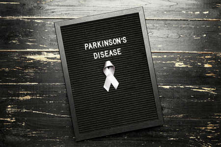 Board with text PARKINSON'S DISEASE and awareness ribbon on dark backgroundの写真素材