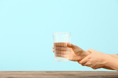 Woman suffering from Parkinson syndrome with glass of water against color backgroundの写真素材