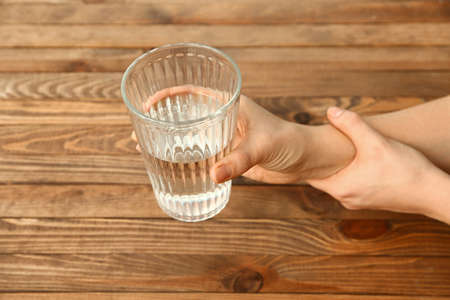 Woman suffering from Parkinson syndrome with glass of water sitting at table, closeupの写真素材