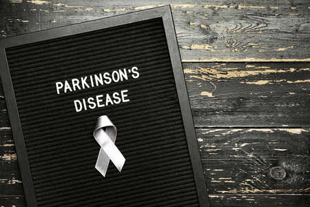 Board with text PARKINSON'S DISEASE and awareness ribbon on dark backgroundの写真素材