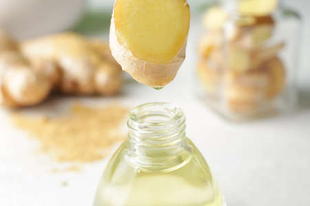 Dripping of ginger essential oil into bottle on table, closeup