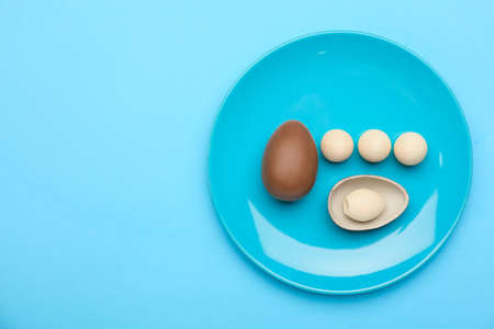 Plate with chocolate Easter eggs on color background