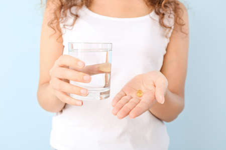 Young woman with fish oil and glass of water on color background, closeupの写真素材