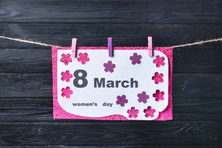 Greeting card for International Women's Day hanging on rope against wooden background