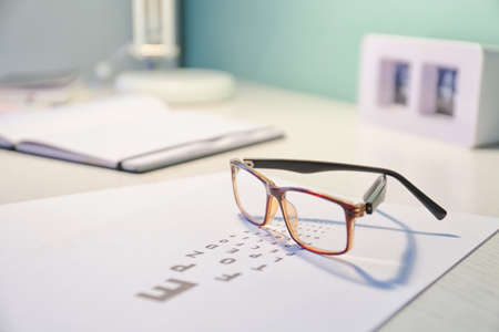 Glasses with eye test chart on table in ophthalmology clinic