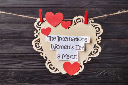 Greeting card for International Women's Day hanging on rope against wooden background