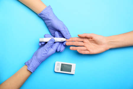 Doctor taking blood sample of diabetic patient on color backgroundの写真素材