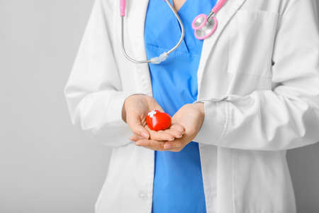 Female cardiologist with red heart on light background