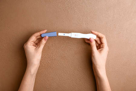 Female hands with pregnancy test on color background