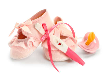 Pregnancy test, baby booties and pacifier on white background