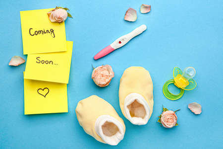 Composition with pregnancy test and baby booties on color background