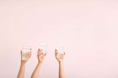 Female hands with glasses of water on color backgroundの写真素材