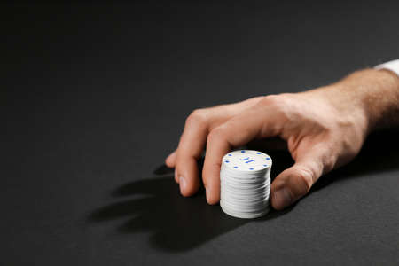 Male hand with chips for gambling games on dark backgroundの写真素材