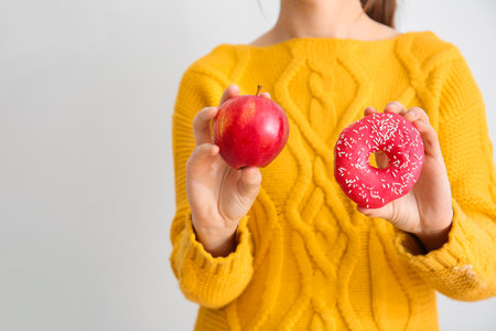 Woman with sweet donut and apple on light backgroundの写真素材