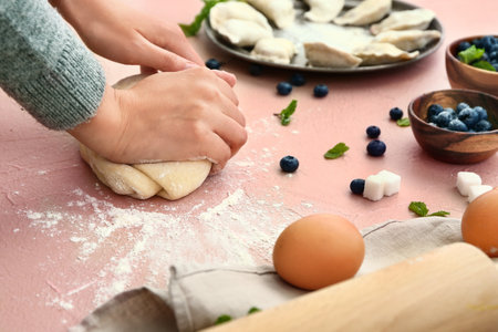 Woman cooking tasty dumplings on color background