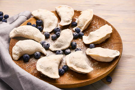 Plate with raw dumplings and blueberries on wooden backgroundの写真素材