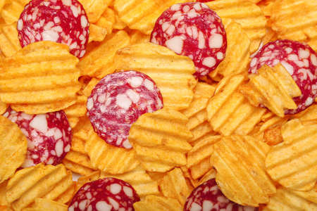 Tasty potato chips with sausages as background