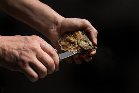 Man opening shell of fresh oyster on dark backgroundの写真素材