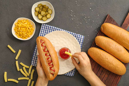 Woman eating tasty hot dog and french fries at table