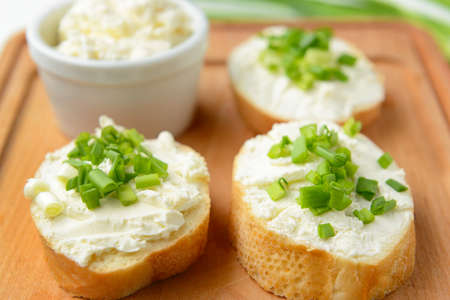 Slices of tasty bread with cream cheese and green onion on board, closeupの写真素材