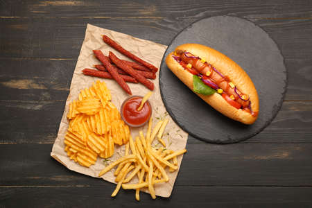 Tasty hot dog, french fries, chips and sauce on table
