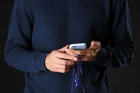 Man with blue earphones and mobile phone on dark backgroundの写真素材