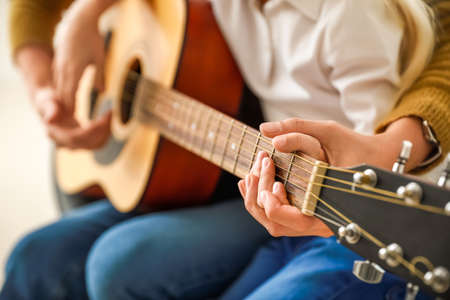 Private music teacher giving guitar lessons to little girl at home, closeup