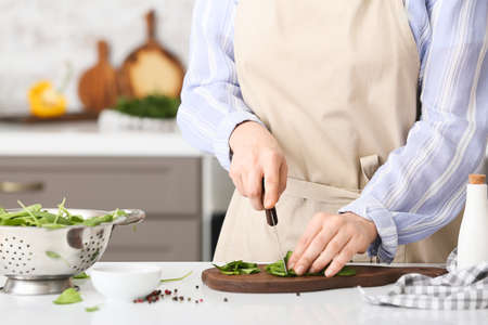 Woman cutting fresh spinach at table in kitchenの写真素材