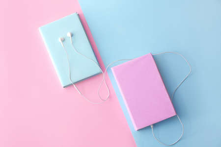 Books and modern earphones on color background. Concept of audiobook