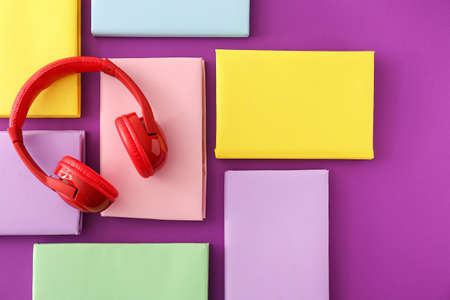Books and modern headphones on color background. Concept of audiobook