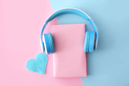 Book and modern headphones on color background. Concept of audiobookの写真素材