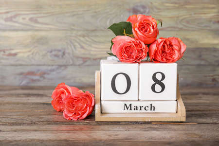 Calendar with date of International Women's Day and flowers on wooden background