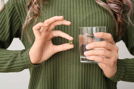 Young woman with fish oil on light background, closeup