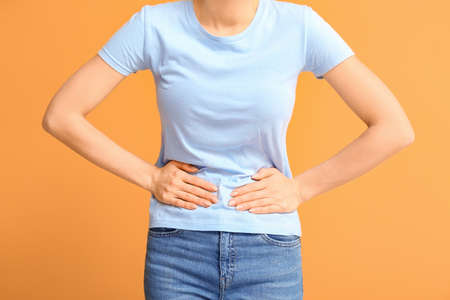 Young woman suffering from menstrual cramps on color backgroundの写真素材
