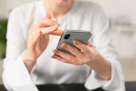 Young woman with mobile phone in office, closeupの写真素材