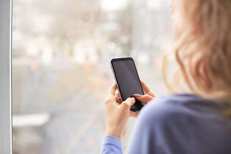 Young woman with mobile phone near window