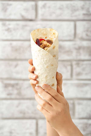 Female hands with tasty doner kebab on brick backgroundの写真素材