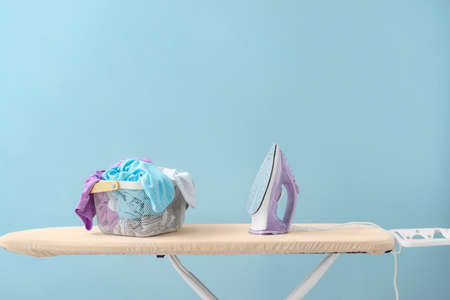Electric iron and board on color background