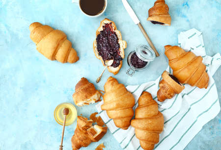 Tasty sweet croissants with jam, honey and coffee on color backgroundの写真素材
